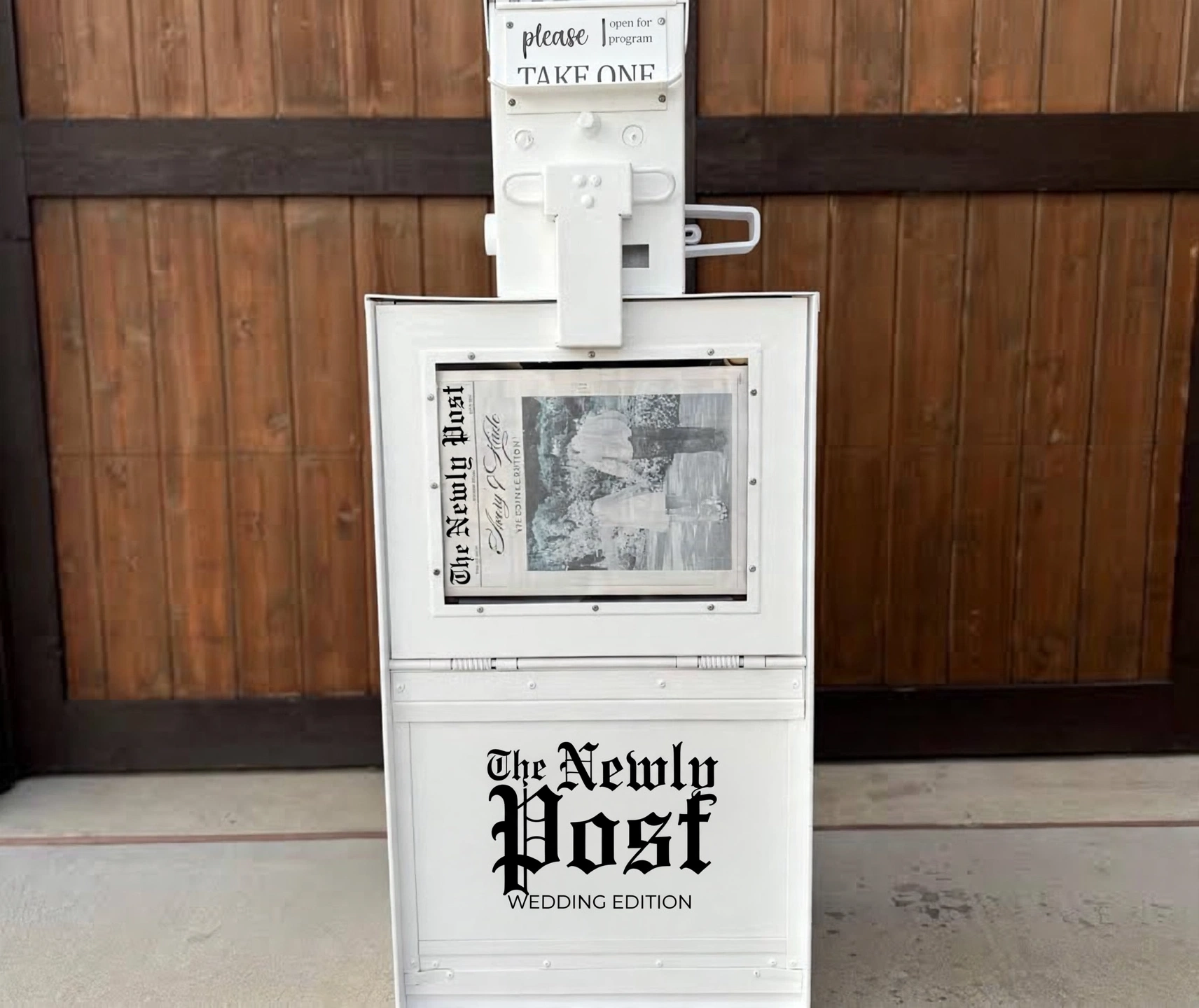 The Newly Post vintage newspaper vending machine — white stand with a sample wedding newspaper in the window and the Wedding Edition masthead on the door